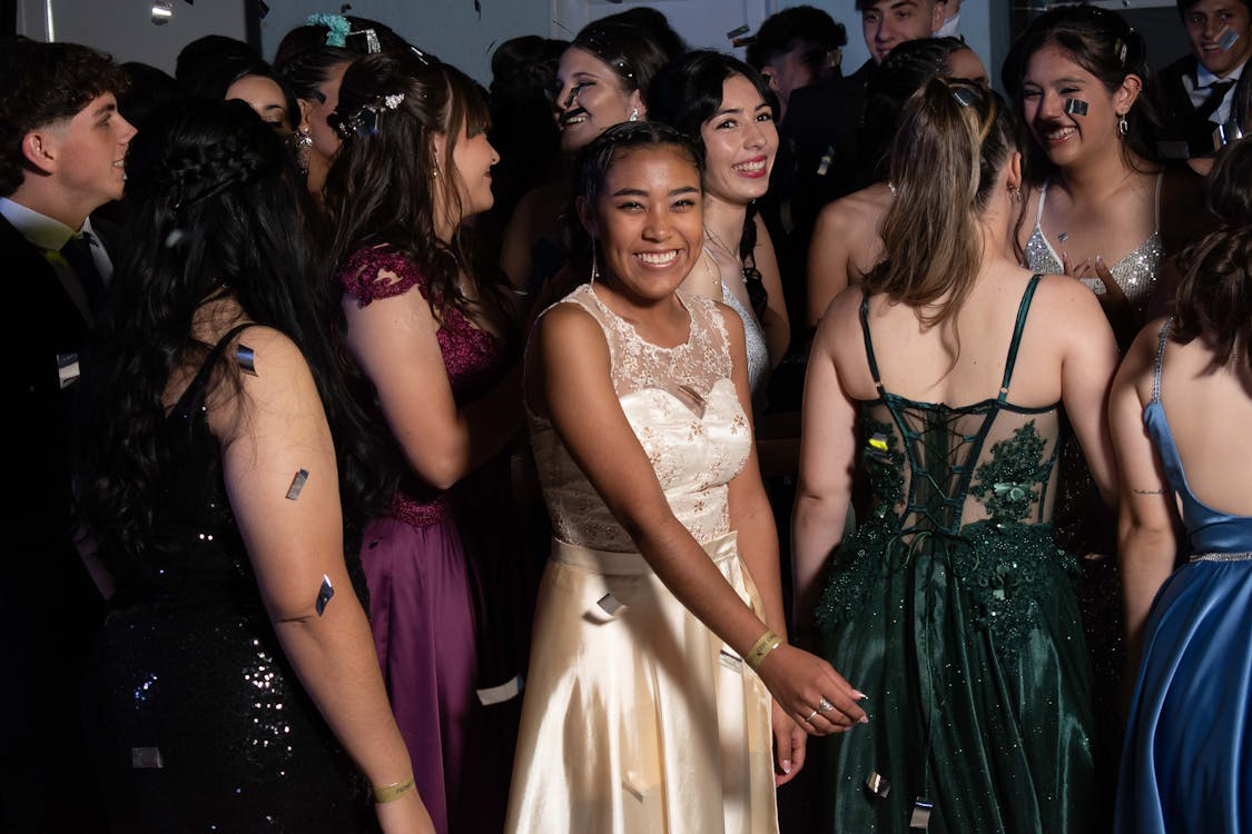 A Girl in a Prom Dress Smiles for the Camera as Students Around Her Dance at a School Event