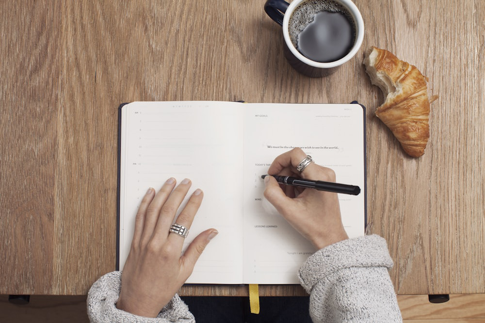 A Woman with a Coffee Mug and Croissant Drafts a Budget for a School Event