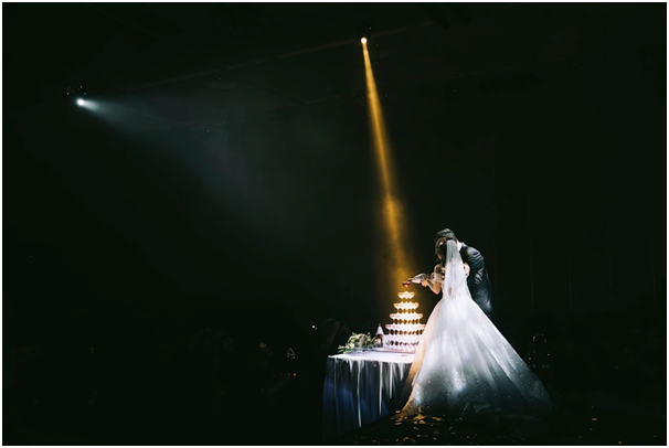 Two Pinspot Wedding Lights Highlight a Couple Pouring Champagne Into a Glass Tower