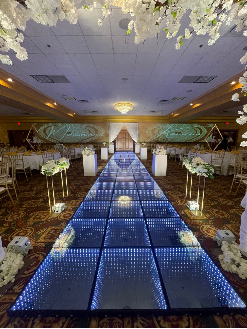 An illuminated 3D infinity LED walkway leading to a wedding stage with floral arrangements and custom monogram wall projections in Cleveland.