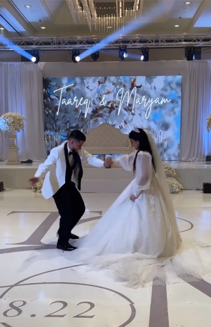Bride and groom dancing on a custom monogrammed dance floor wrap with moving head stage lighting beams behind them.