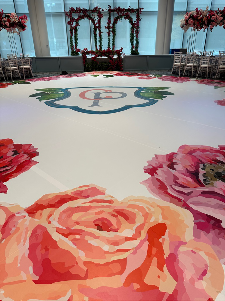 White vinyl dance floor wrap printed with vibrant pink floral illustrations and a centered wedding crest monogram.